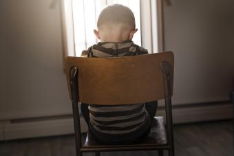 child sitting alone in a chair with back to viewer and their head is pointed downward